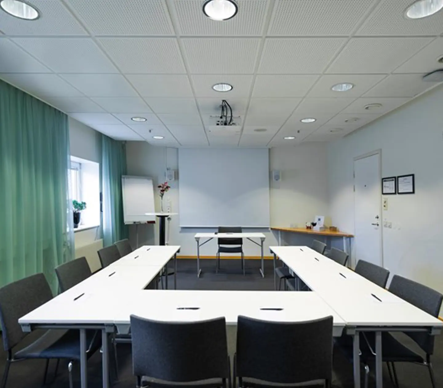 Conference room with U-shaped seating, green curtains, white table and gray chairs