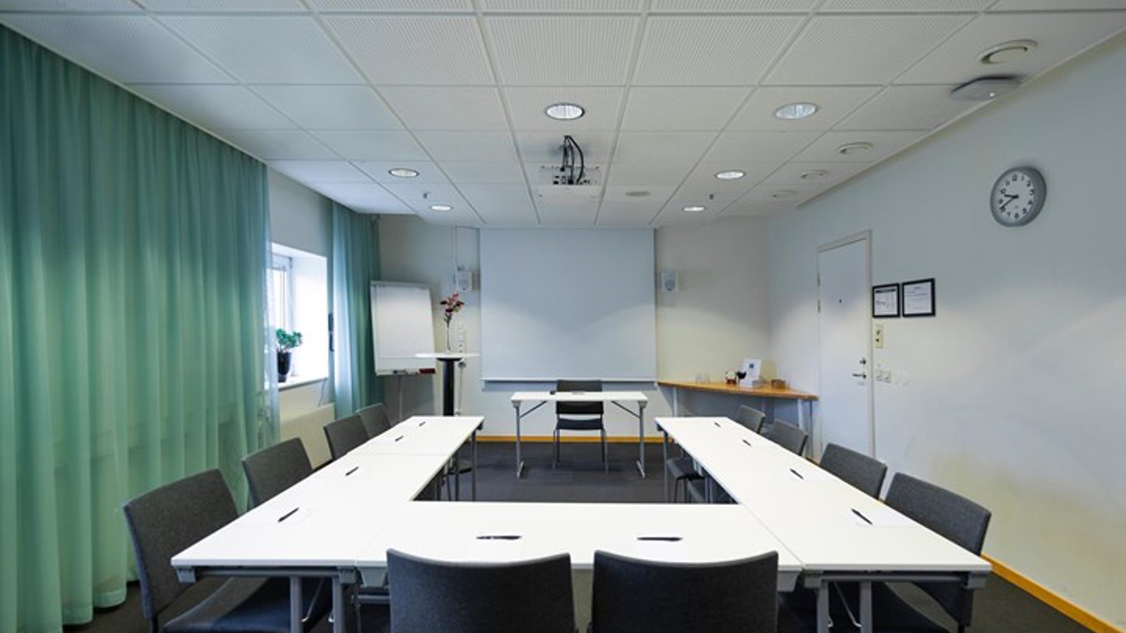 Conference room with U-shaped seating, green curtains, white table and gray chairs