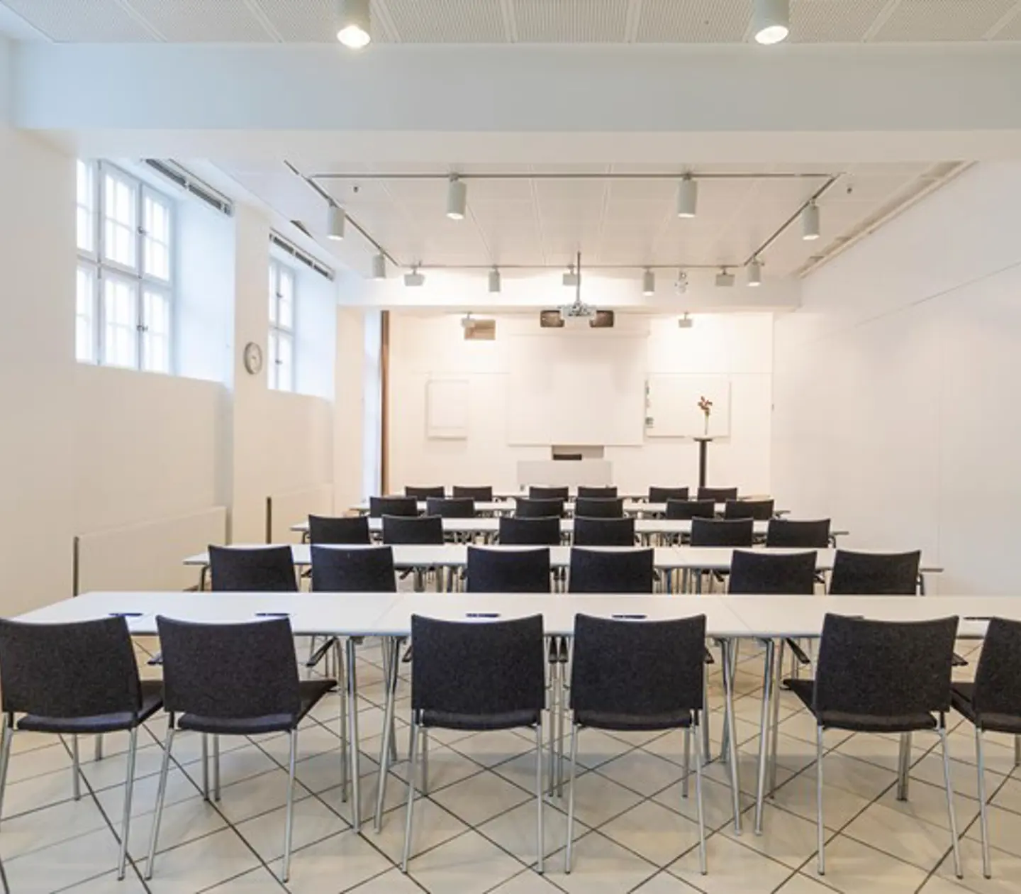 White conference room with school seating, dark chairs and several windows