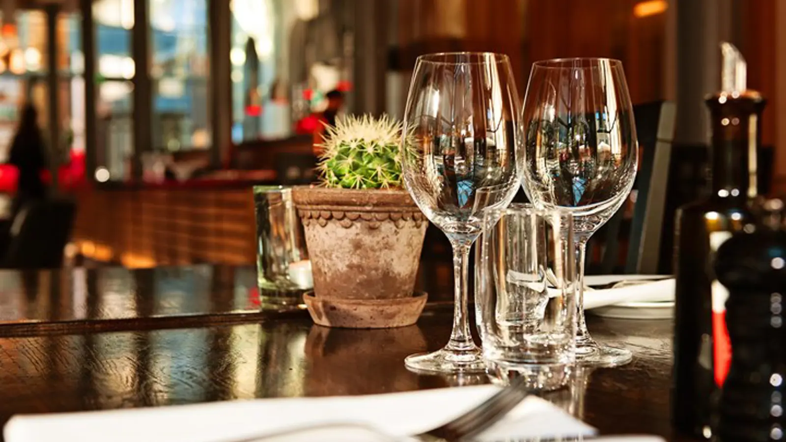 Närbild på dukat bord med vinglad och bestick i förgrunden, restaurangmiljö och fönster i bakgrunden
