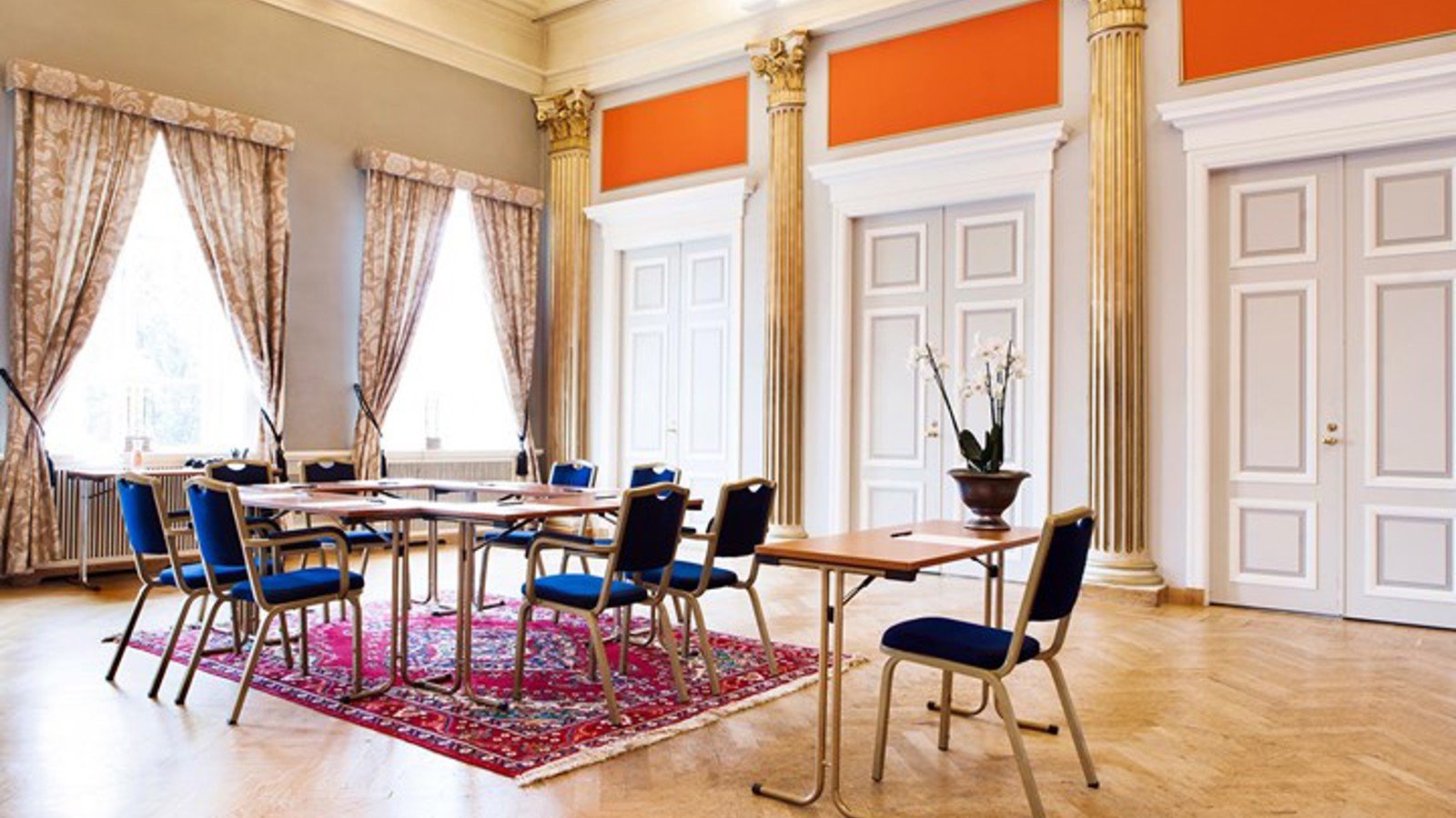Conference room with high ceiling, gold pillars, large windows and blue chairs