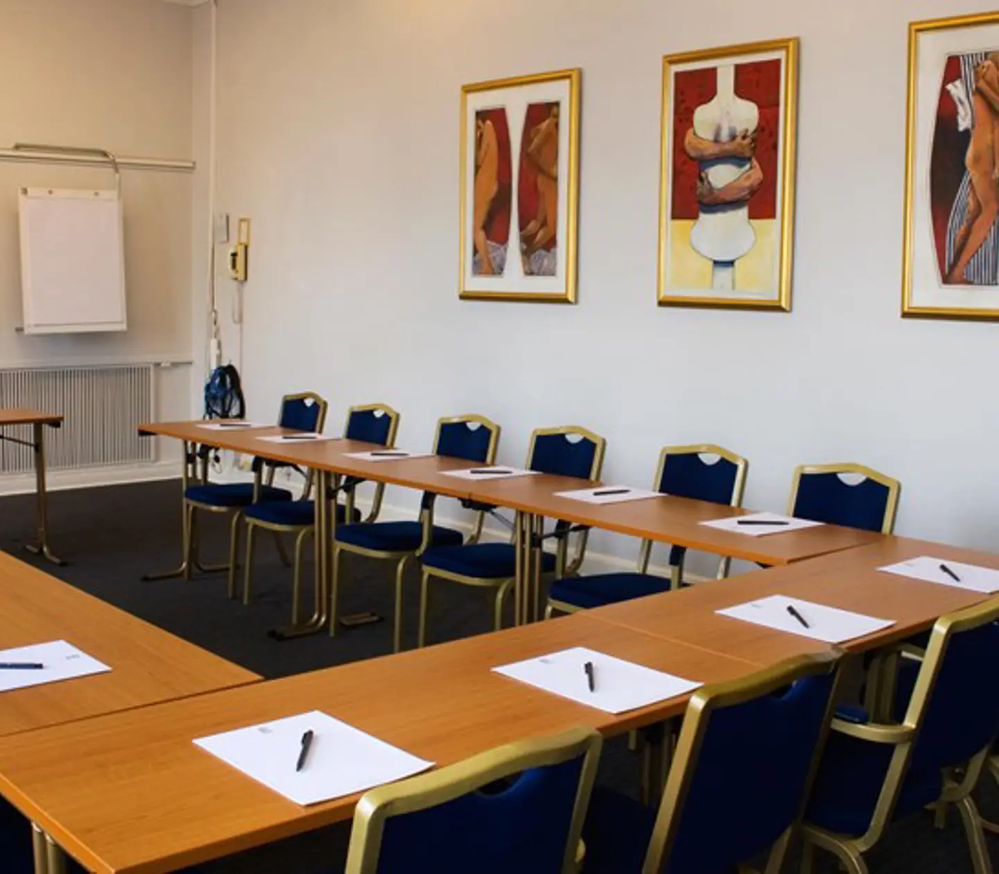 Konferensrum med u-sittning, träbord, mörkt golv och tavlor