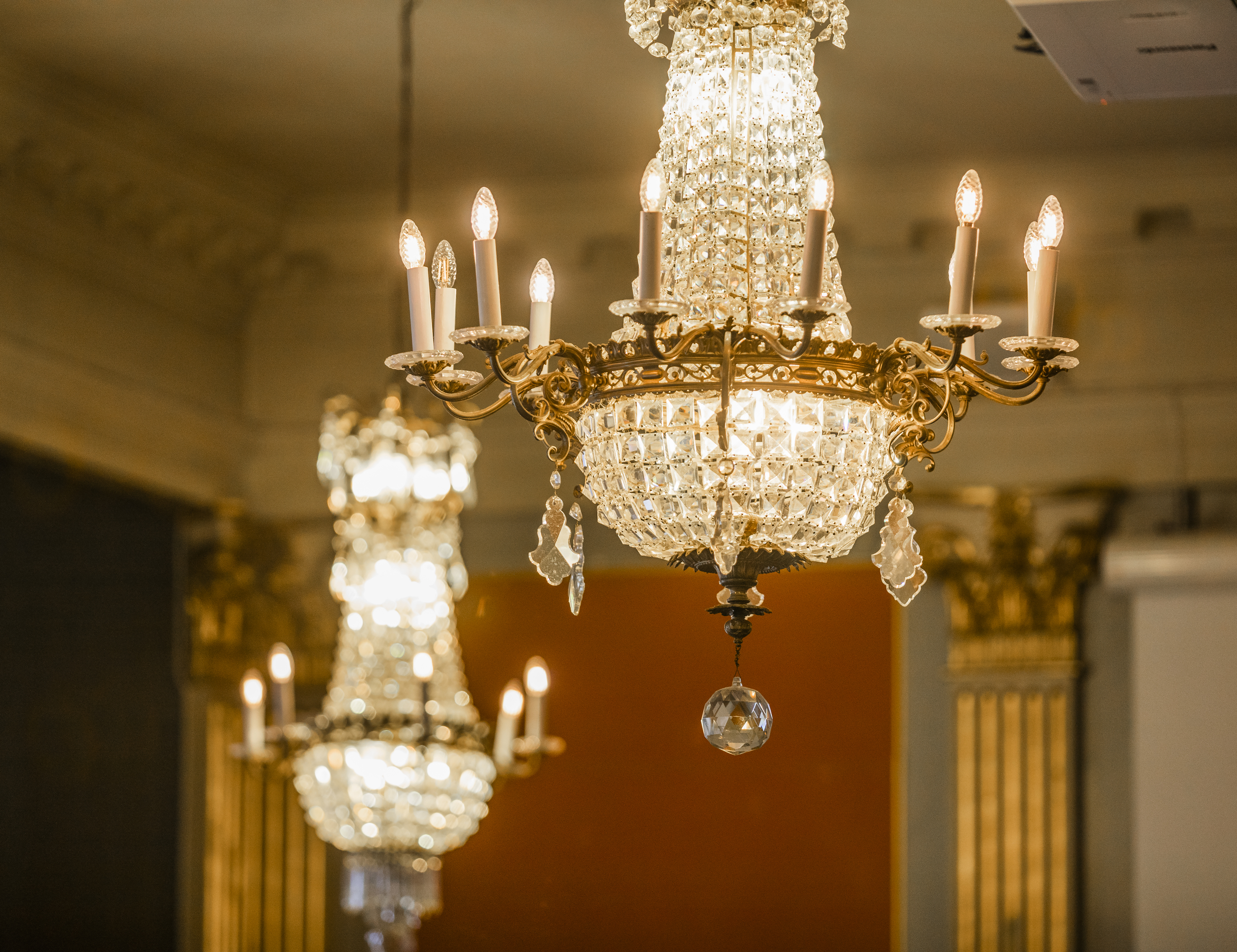 Elegant crystal chandeliers with lit candles in a grand ballroom setting, featuring ornate gold detailing and ambient lighting.