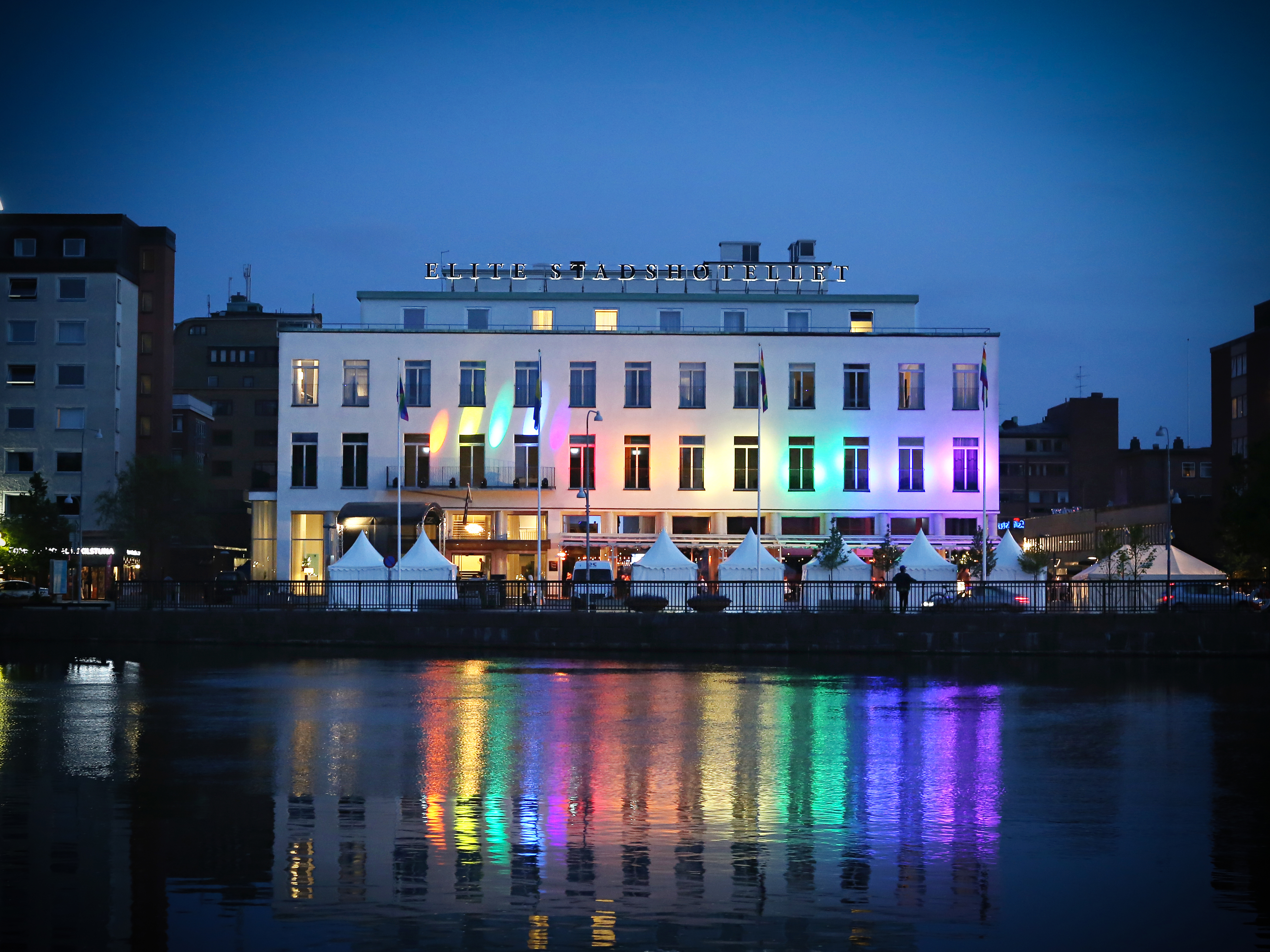 En magnifik byggnad lyser upp i regnbågsfärger som speglar sig i sjön