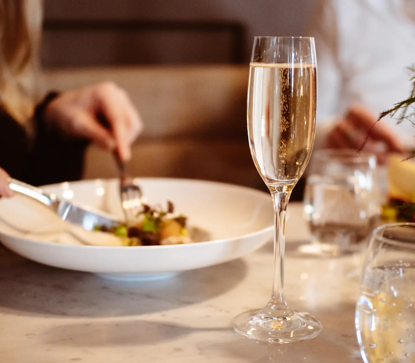 Person äter en fräsch middag i en elegant restaurang, med ett glas champagne framför sig på en marmorbordsskiva.