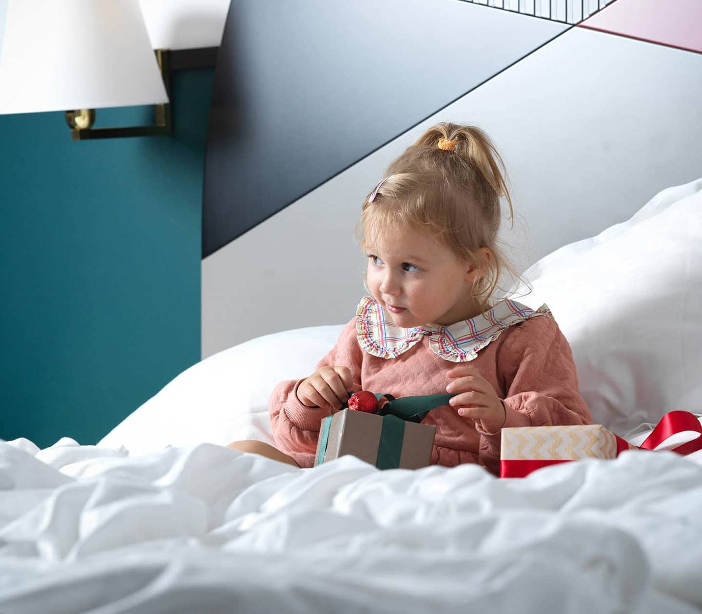 A child sitting on a hotel bed opening Christmas gifts 