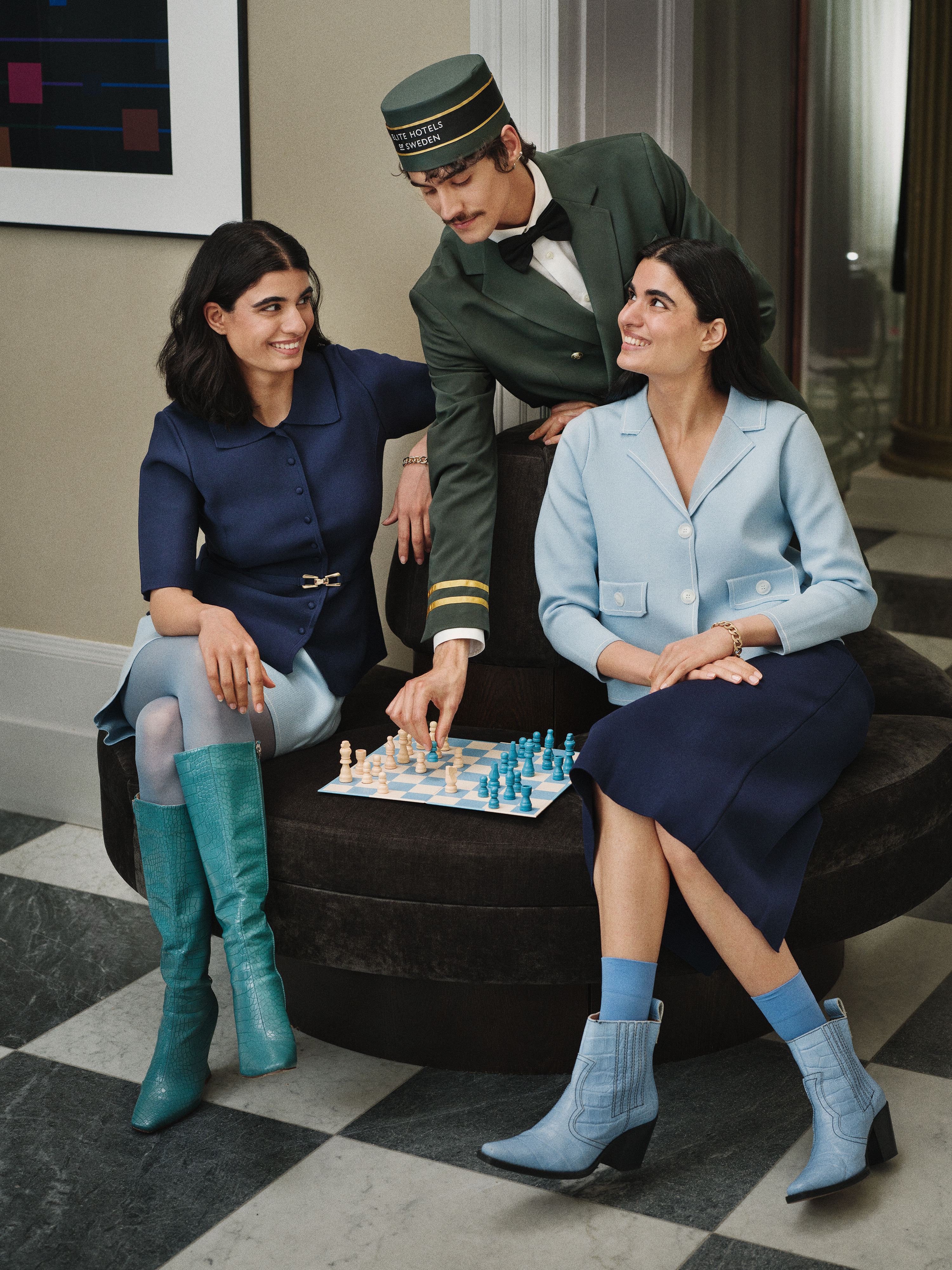 Three people in vintage attire enjoy a game of chess in a stylishly decorated room.