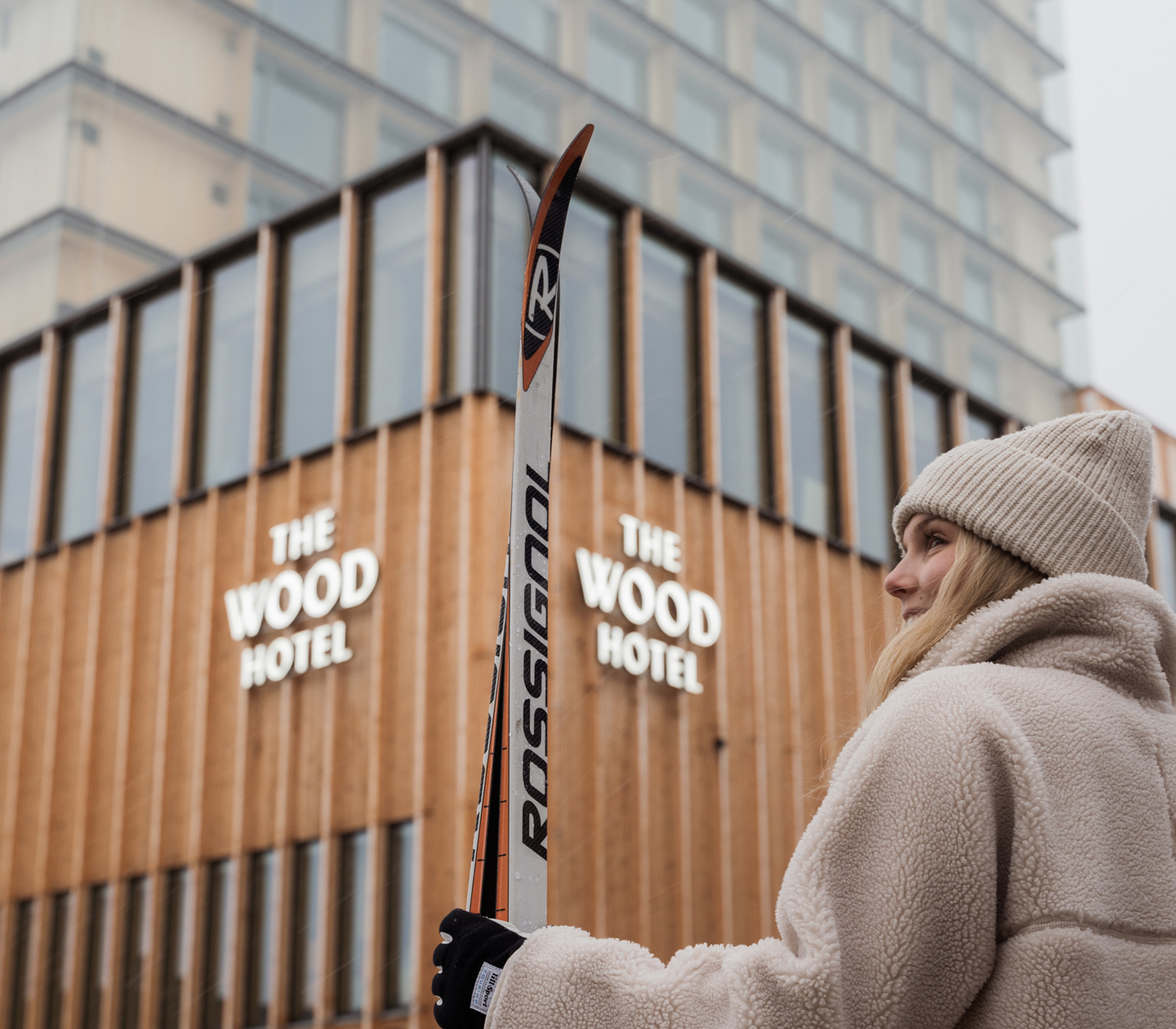 Woman in winter clothes with skis in hand in front of The Wood Hotel