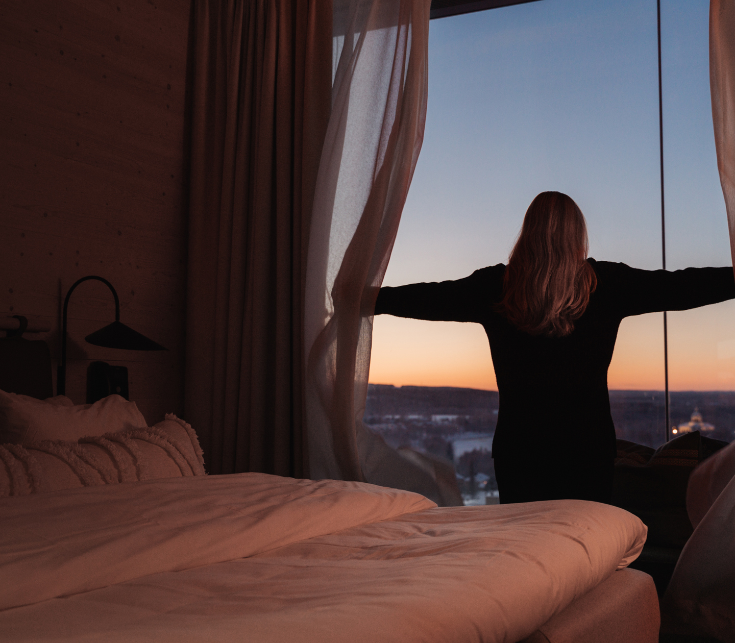 Kvinna framför fönster som håller isär gardiner