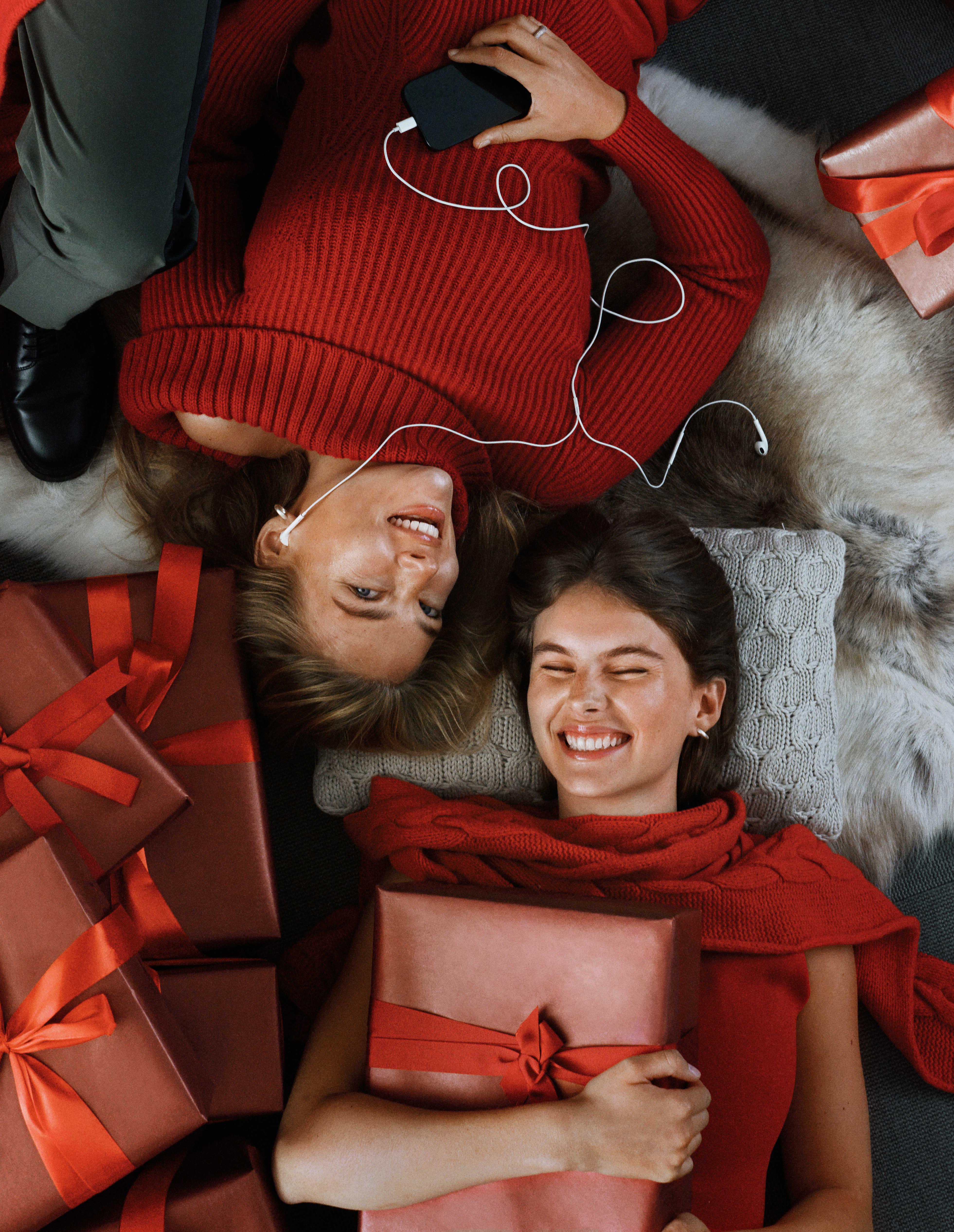 Man in a white cable-knit sweater and scarf sitting in a snowy setting, holding a thermos. Two young children in warm winter clothing and knit hats drink from mugs nearby.