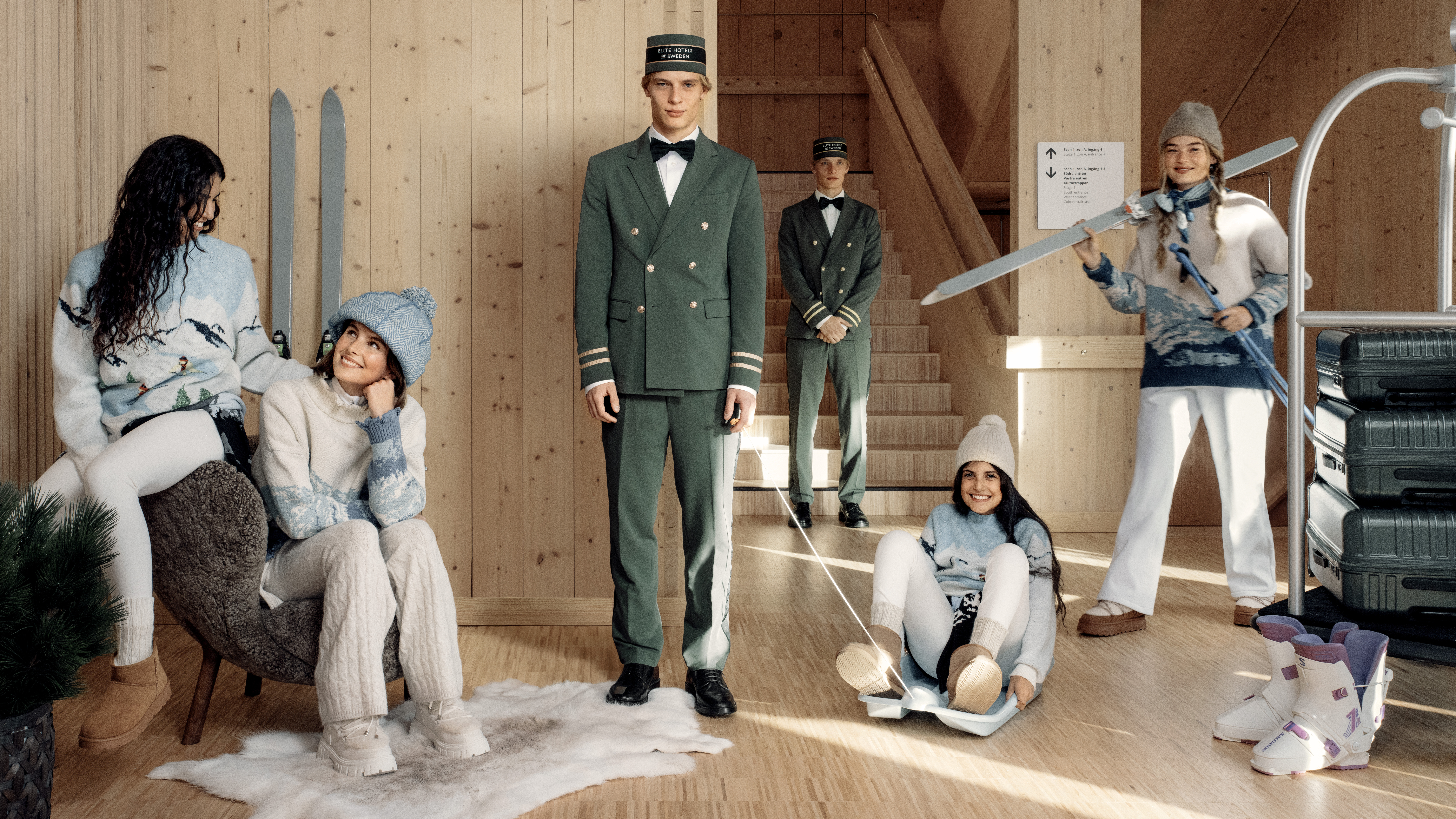 Julscen med människor klädda i rött och vita uniformer, omgivna av staplade julklappar och resväskor. Ett barn och en hund sitter på golvet framför en julgran.