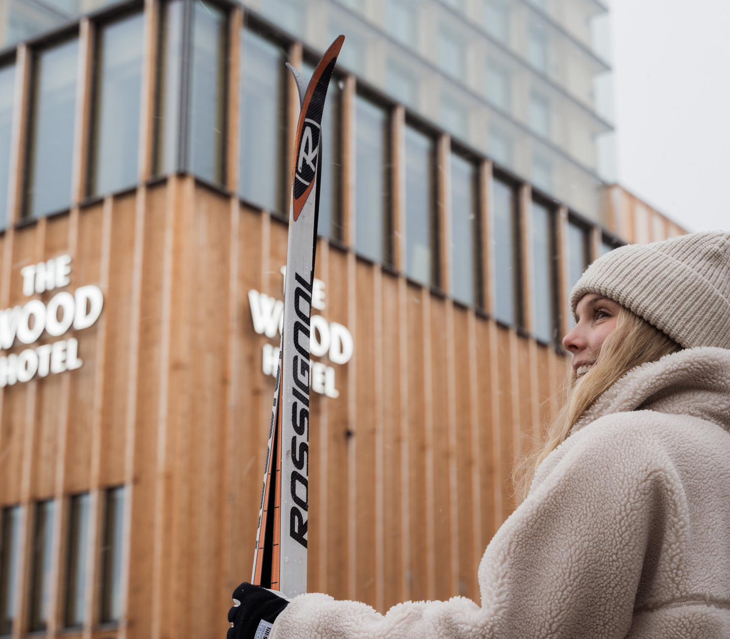 Kvinna som står utanför hotell med skidor i händerna