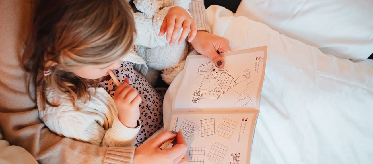 En mamma sitter och ritar i en bok tillsammans med sin dotter.