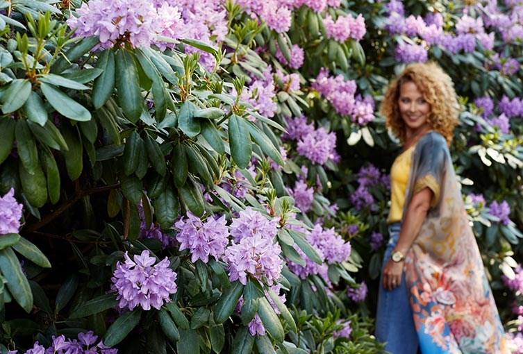 En kvinna i somrig klänning står vid en blommig buske.