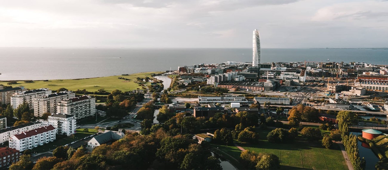 Helikoptervy över Malmö med många bostadshus, Turning Torso och havet i bakgrunden