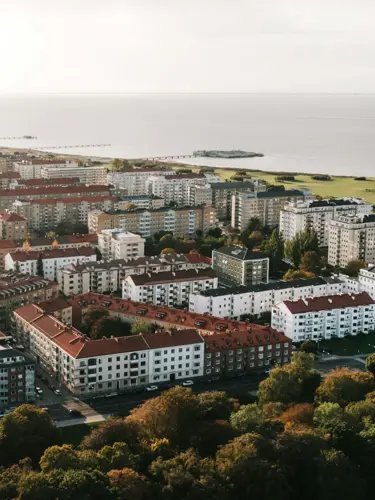 Flygbild över ett bostadsområde i Malmö med havsutsikt, grönområden och flervåningshus med röda tak.