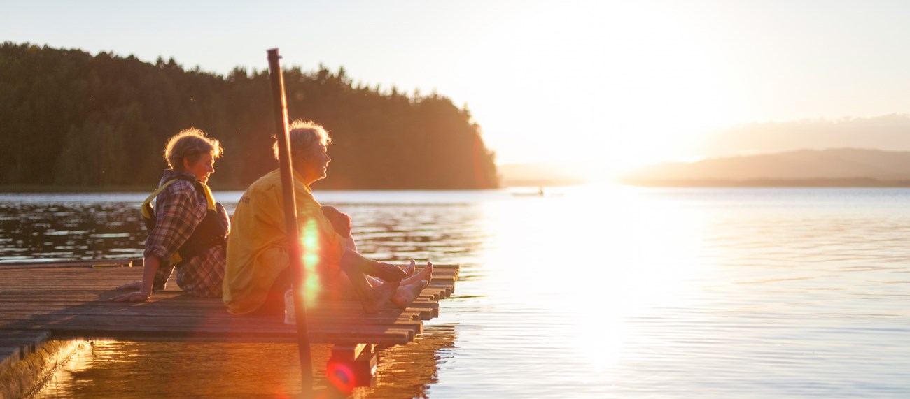 Två personer sitter på en brygga i solnedgången