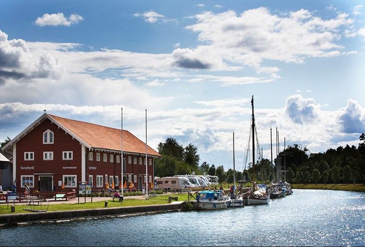 Stort rött hus med husbilar utanför och ett gäng båtar längs en brygga i vattnet