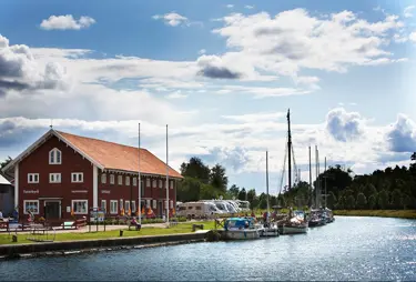 Stort rött hus med husbilar utanför och ett gäng båtar längs en brygga i vattnet