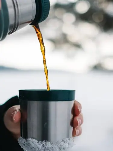 Närbild på hand som häller upp kaffe ur termos