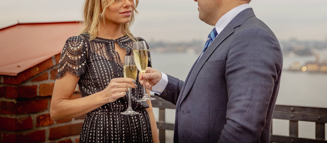 En uppklädd man och kvinna i klänning utbringar en skål med utsikt över stan