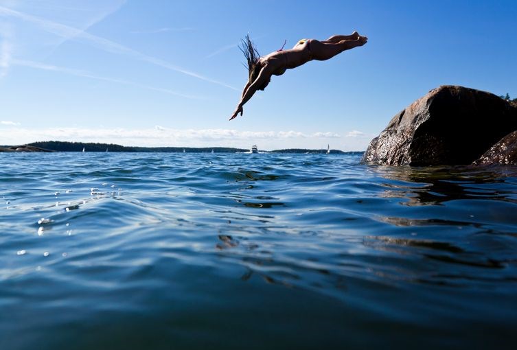 En tjej som dyker ner i vattnet från en klippa