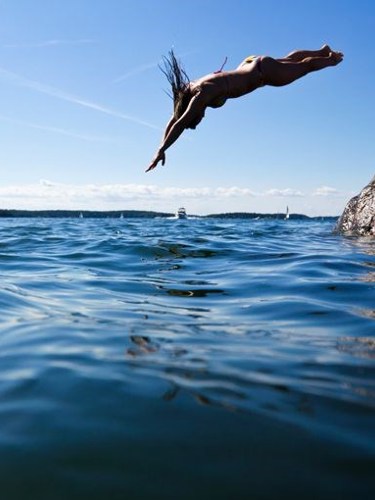 En tjej som dyker ner i vattnet från en klippa