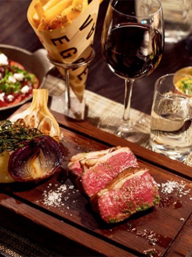 Köttbitar serverad på planka och ett vinglas med rött vin bredvid