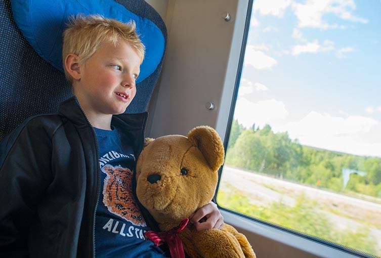 Barn som åker tåg med sin nallebjörn i famnen