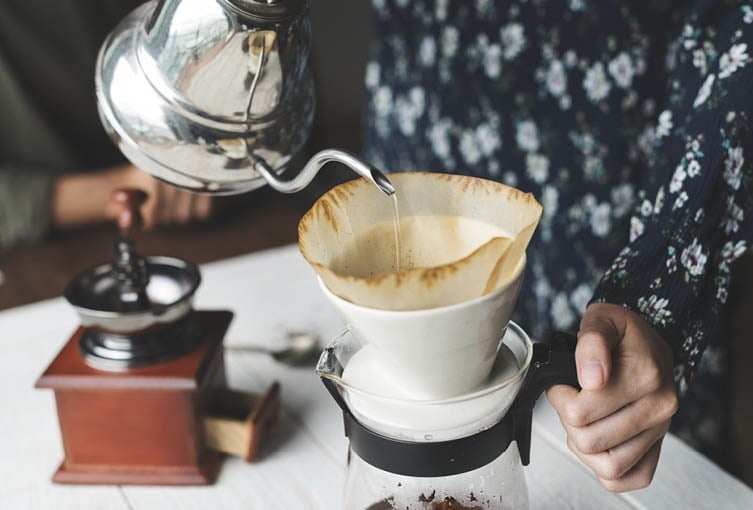 Kokande vatten hälls upp i en kanna med kaffefilter