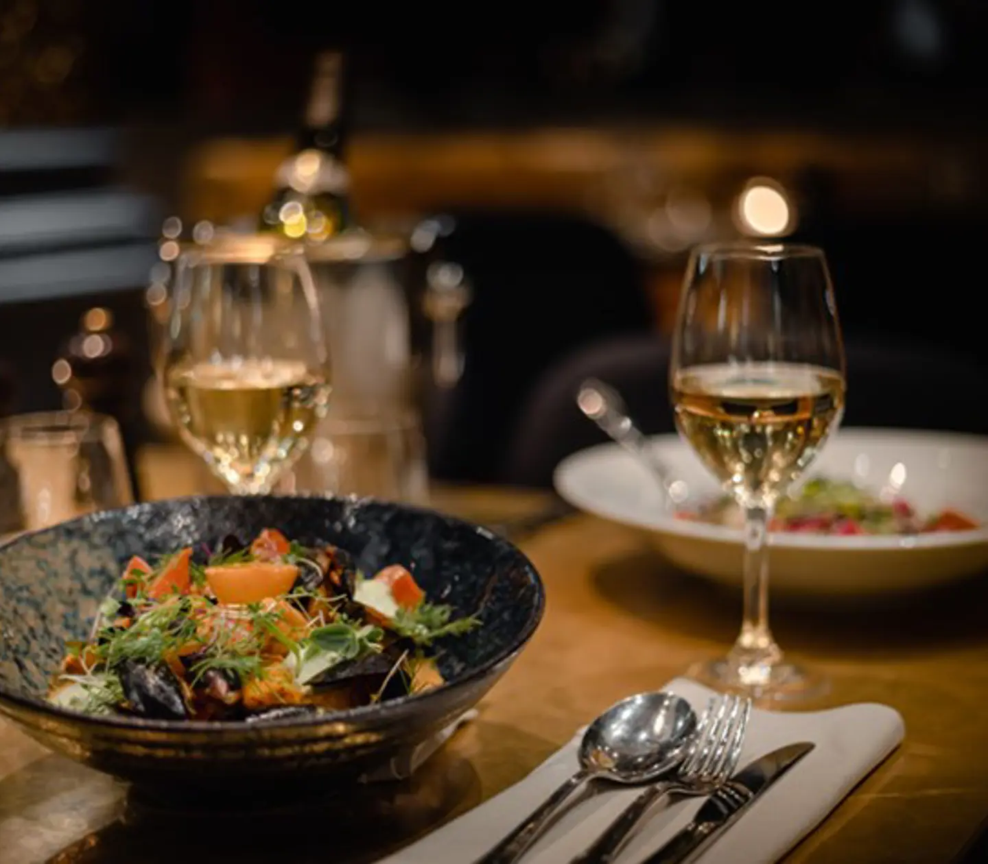 Elegant middagsupplevelse med en skål sallad och ett glas vitt vin på ett dukat bord i en mysig restaurangmiljö med varm belysning.