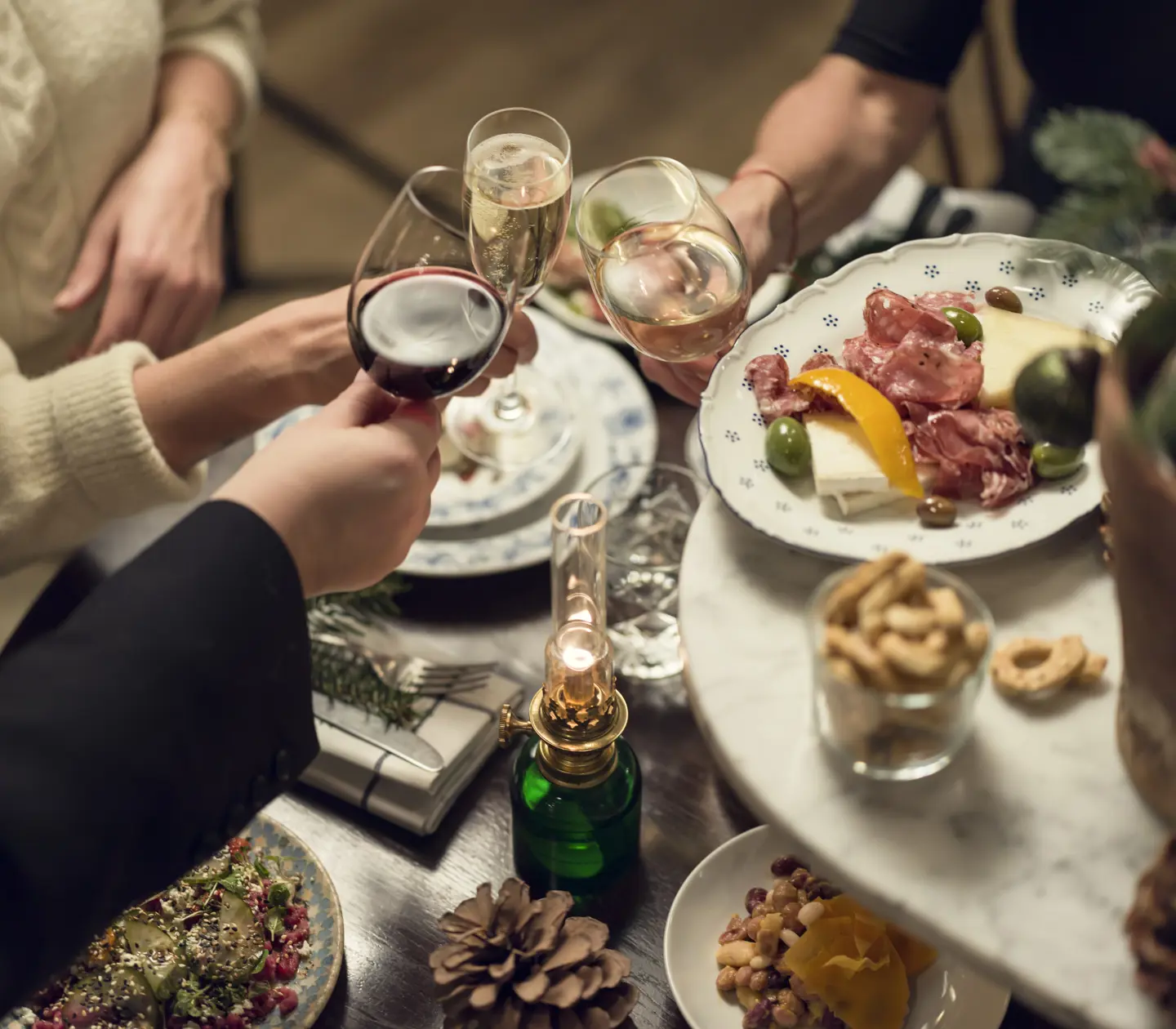 Skål vid middagsbord med vin och delikatessbricka, inklusive charkuterier och oliver.