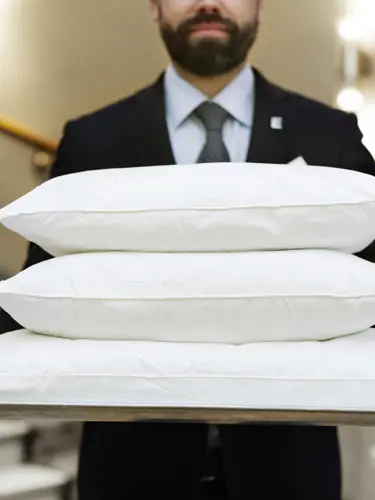 Man in suit carrying three white pillows on tray