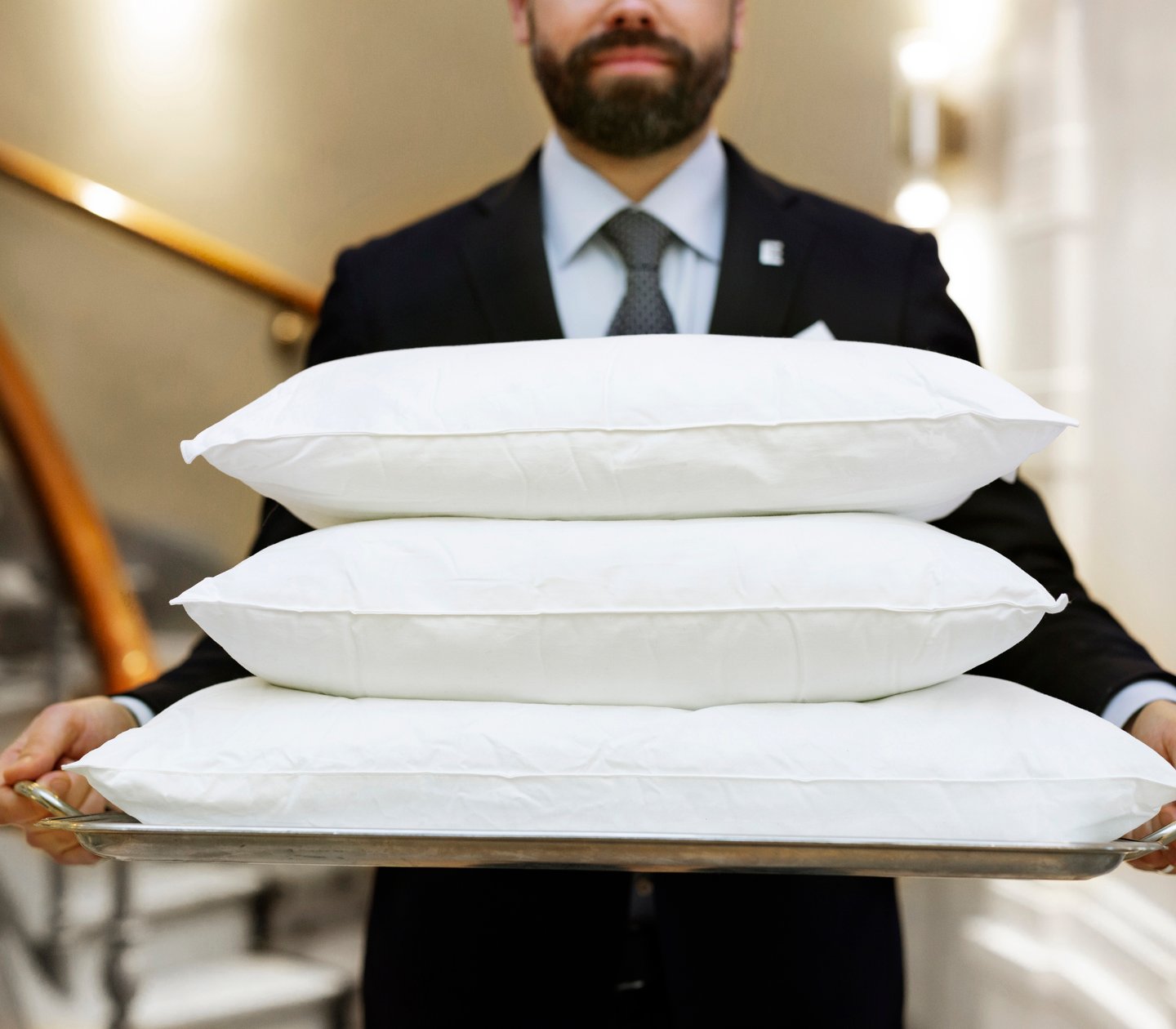 Man in suit carrying three pillows on tray