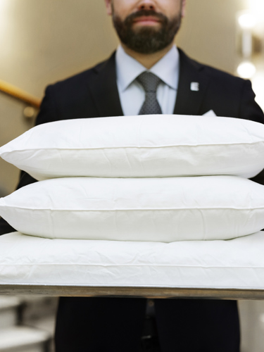 Man in suit carrying three white pillows on tray