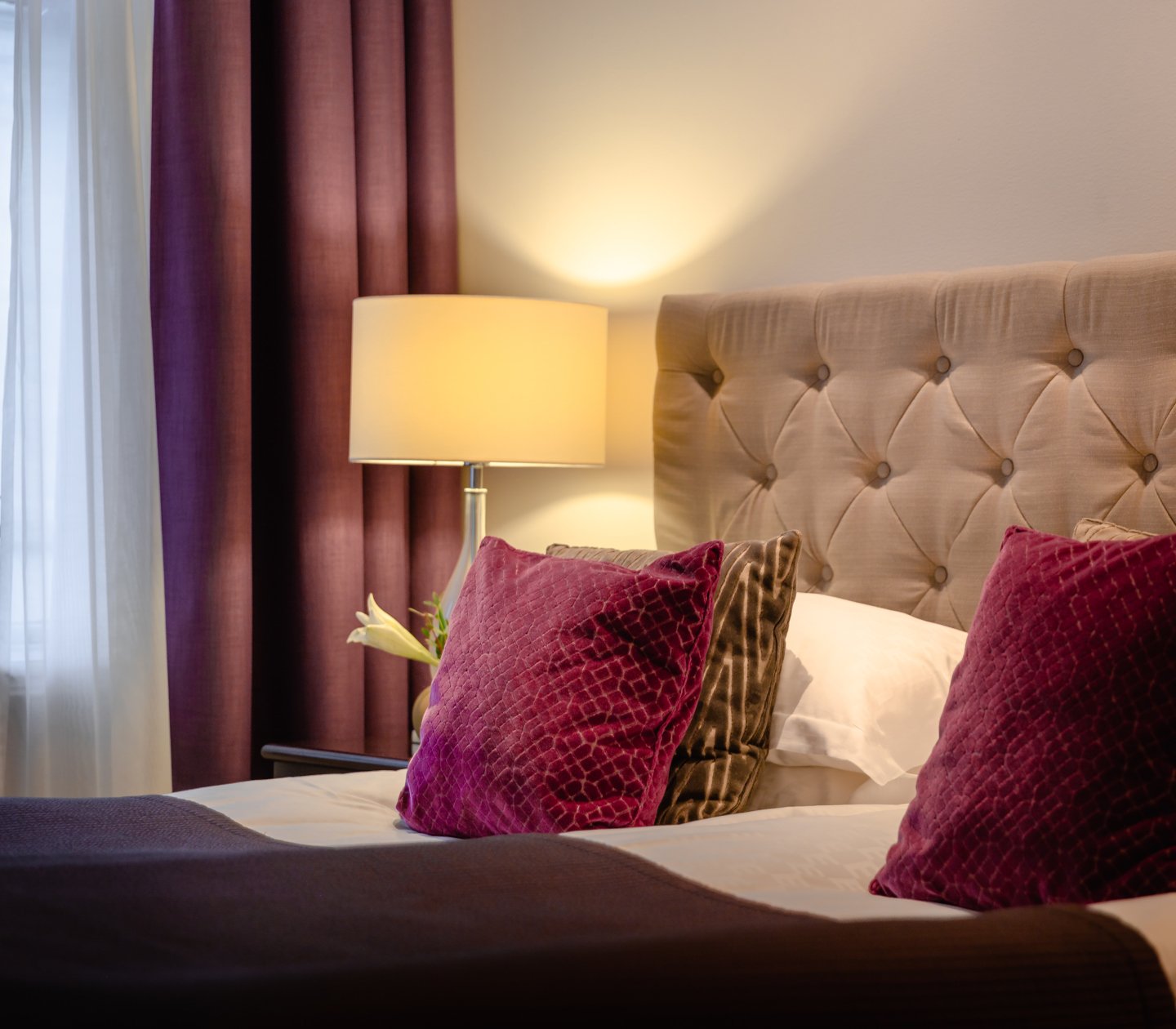 Cozy hotel room with bed, purple pillows and bedside lamp