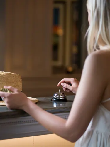 Kvinna i klänning som står i receptionsdisk och ringer på klocka