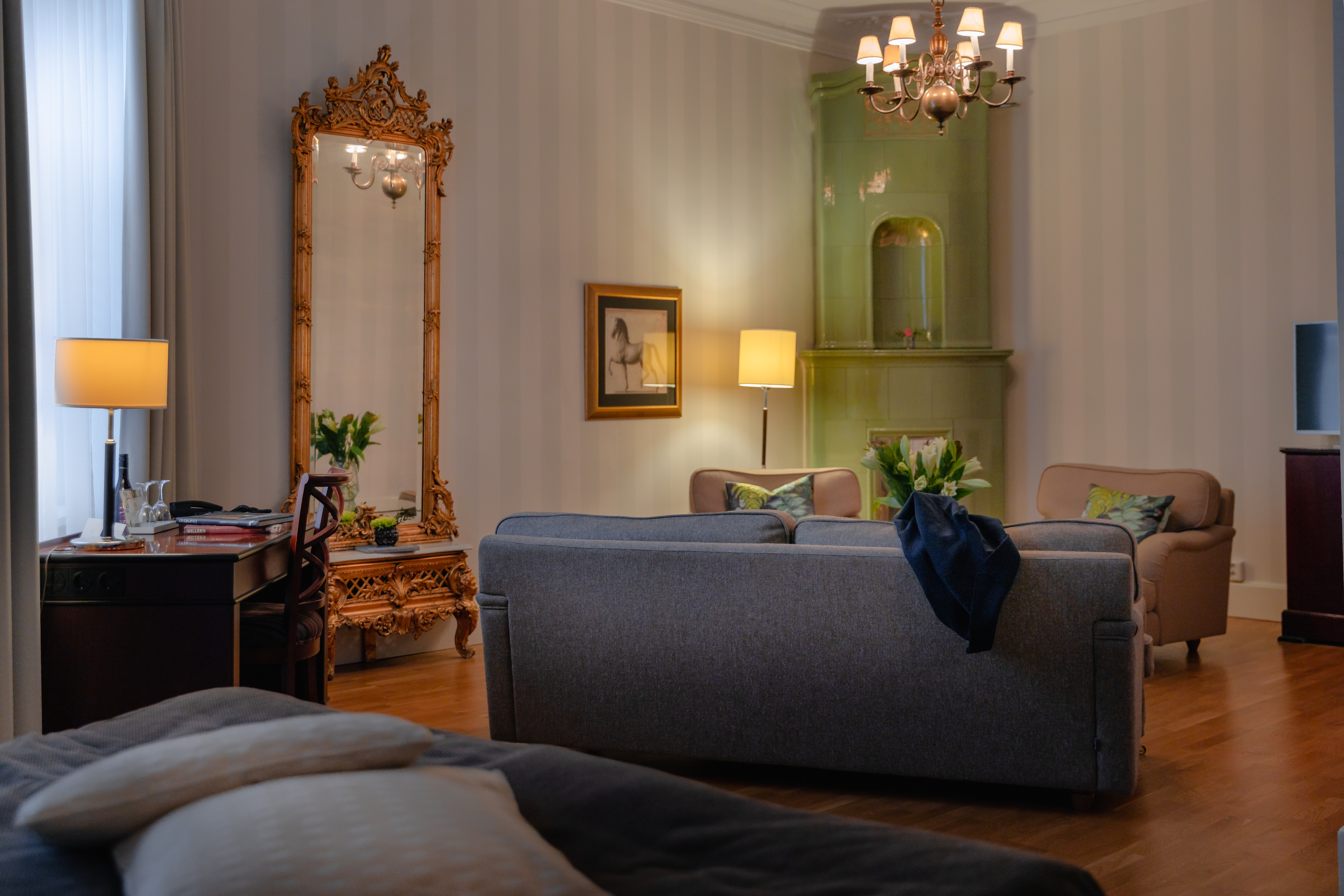 Svit med soffa, guldig spegel och grön kakelugn