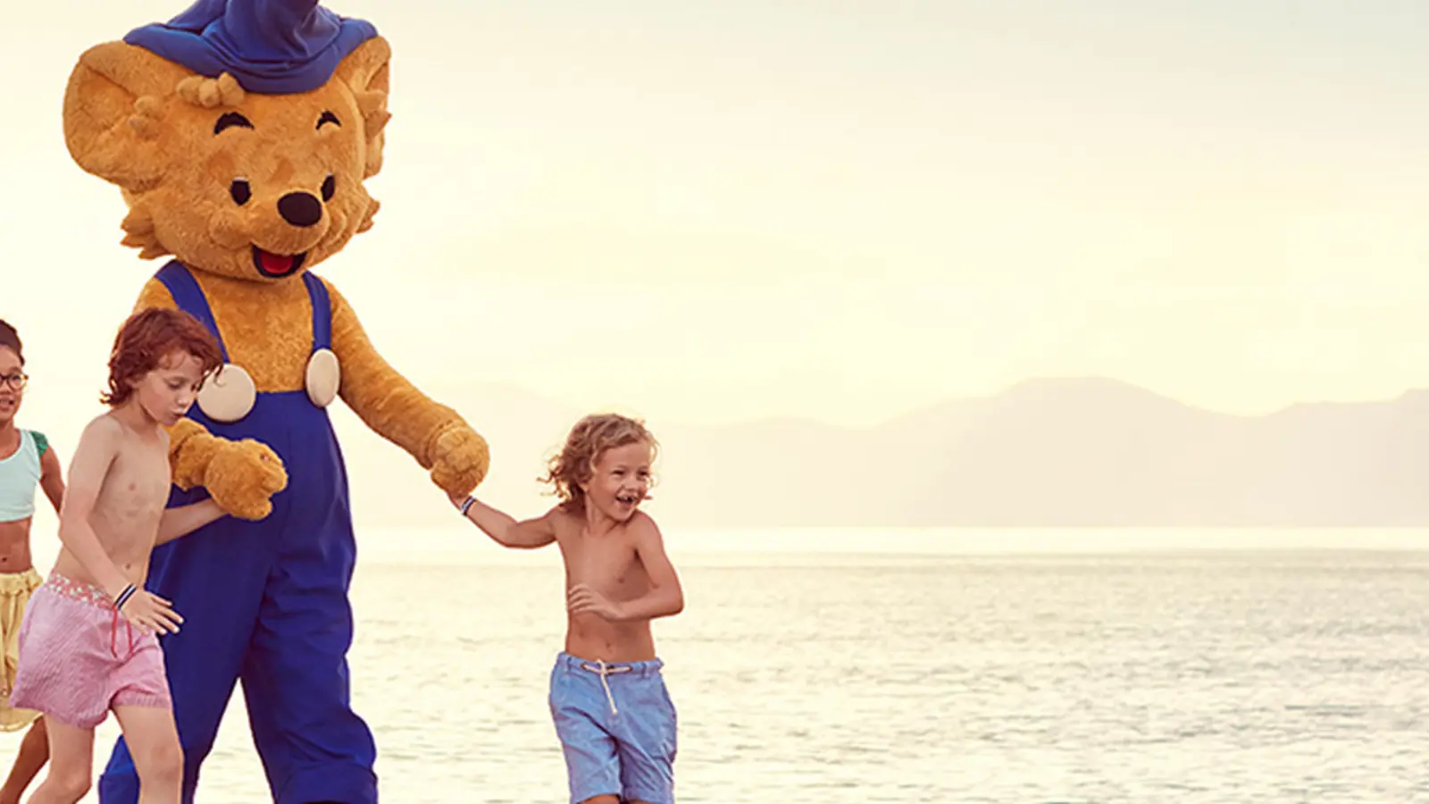 Barn springer på en strand med Bamse