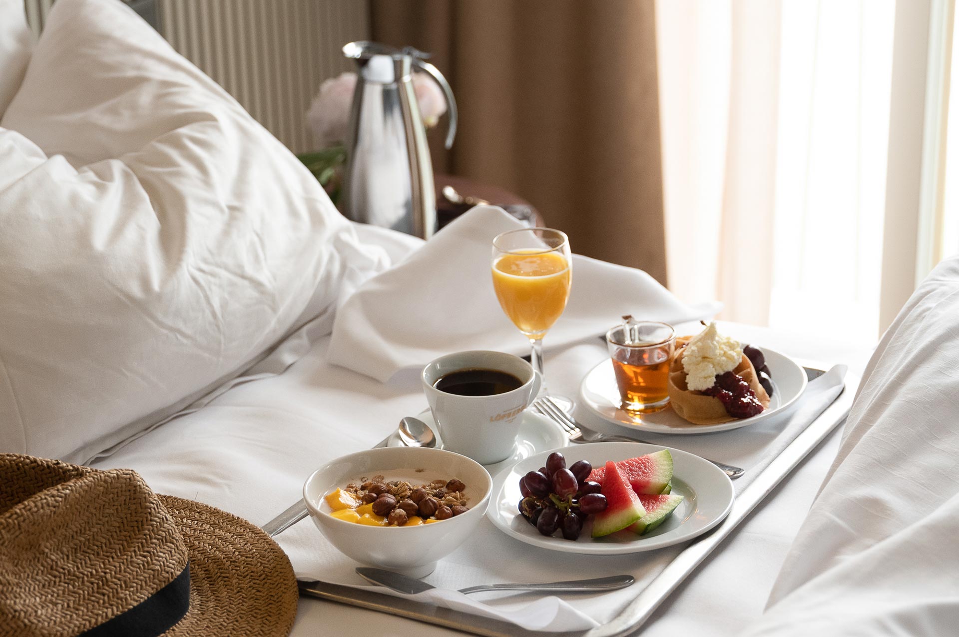 Breakfast tray laid out in a bed and with a straw hat in the foreground