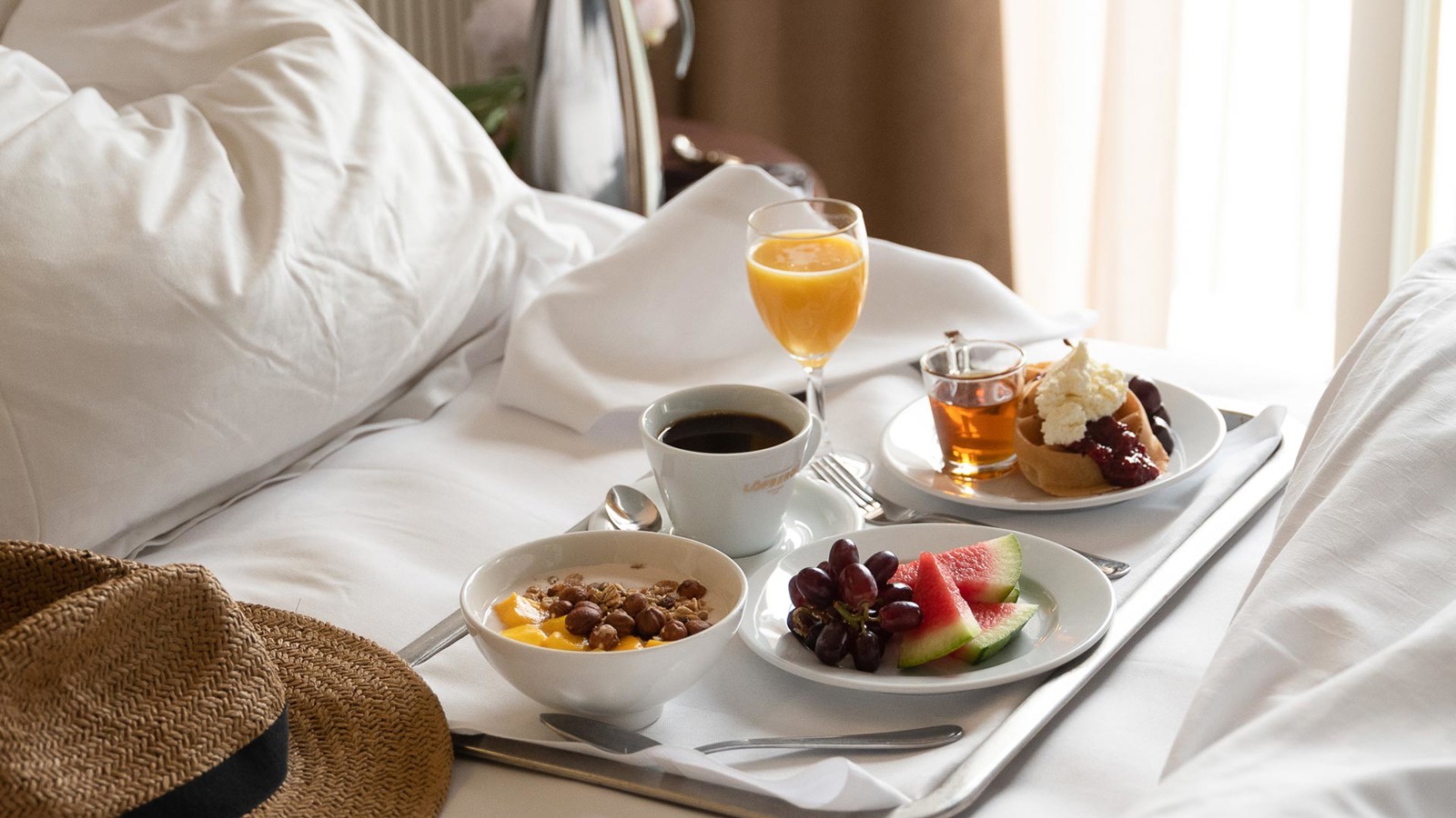 Breakfast tray laid out in a bed and with a straw hat in the foreground