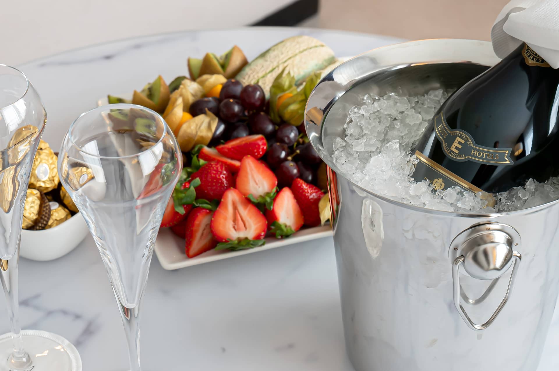 Champagne in an ice bucket, two glasses, chocolate and fruit platter on display