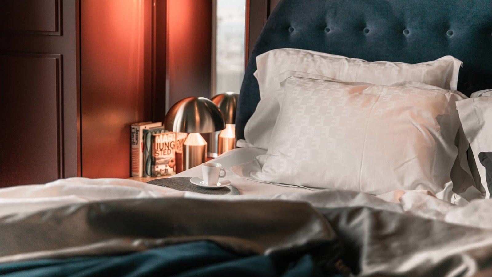 Close-up of hotel bed, coffee cup and bedside lamp