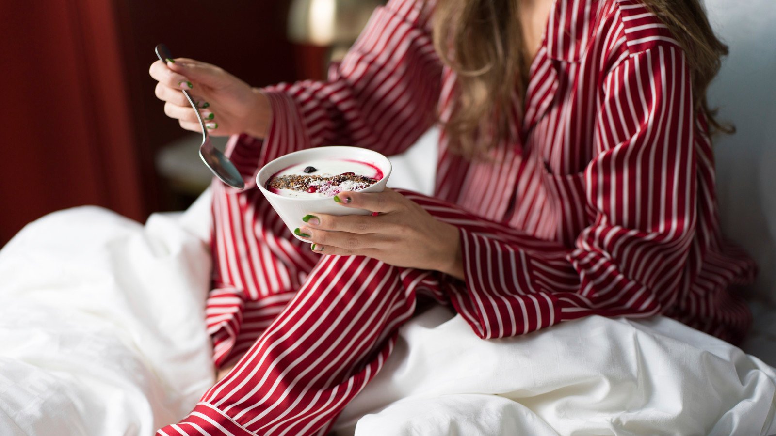 Girl in red and white striped pajamas eating breakfast in hotel bed
