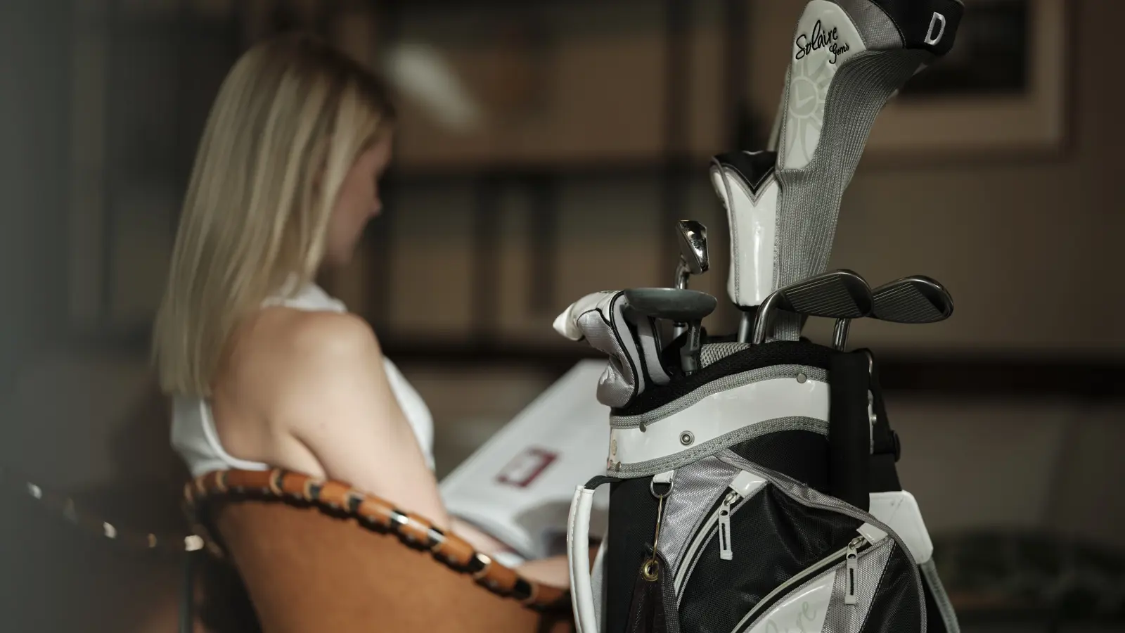 Kvinna sittandes i fåtölj med en bag med golfklubbor