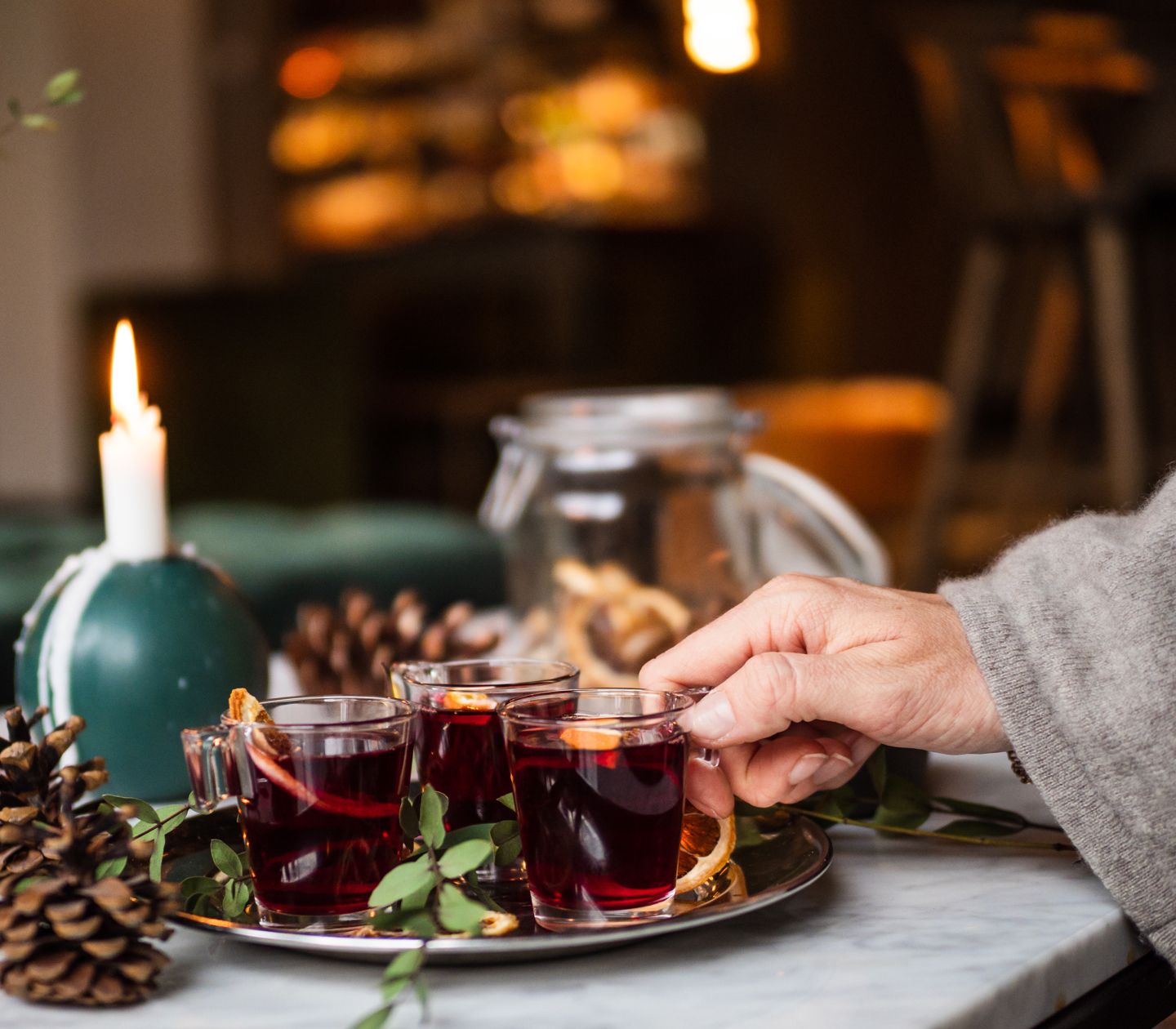 A hand reaching for a glass of mulled wine standing on a golden tray