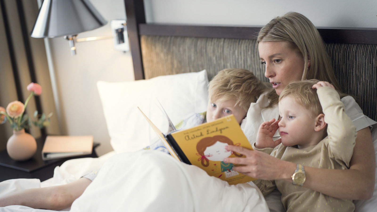 Woman reading book to two children in a bed