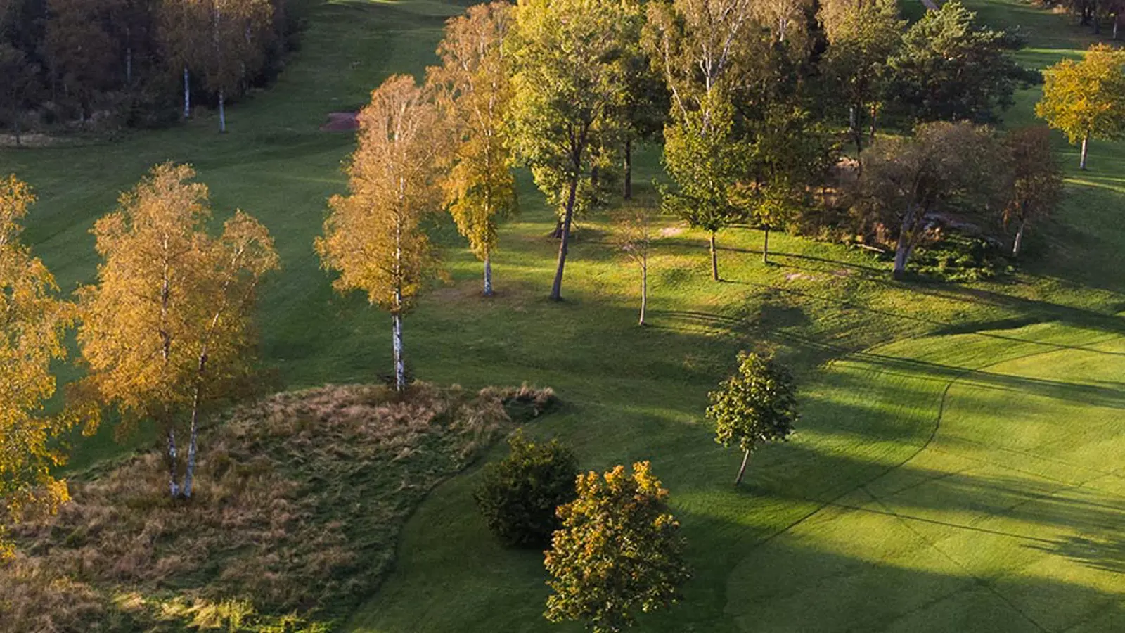 Large golf course with forest groves and pond