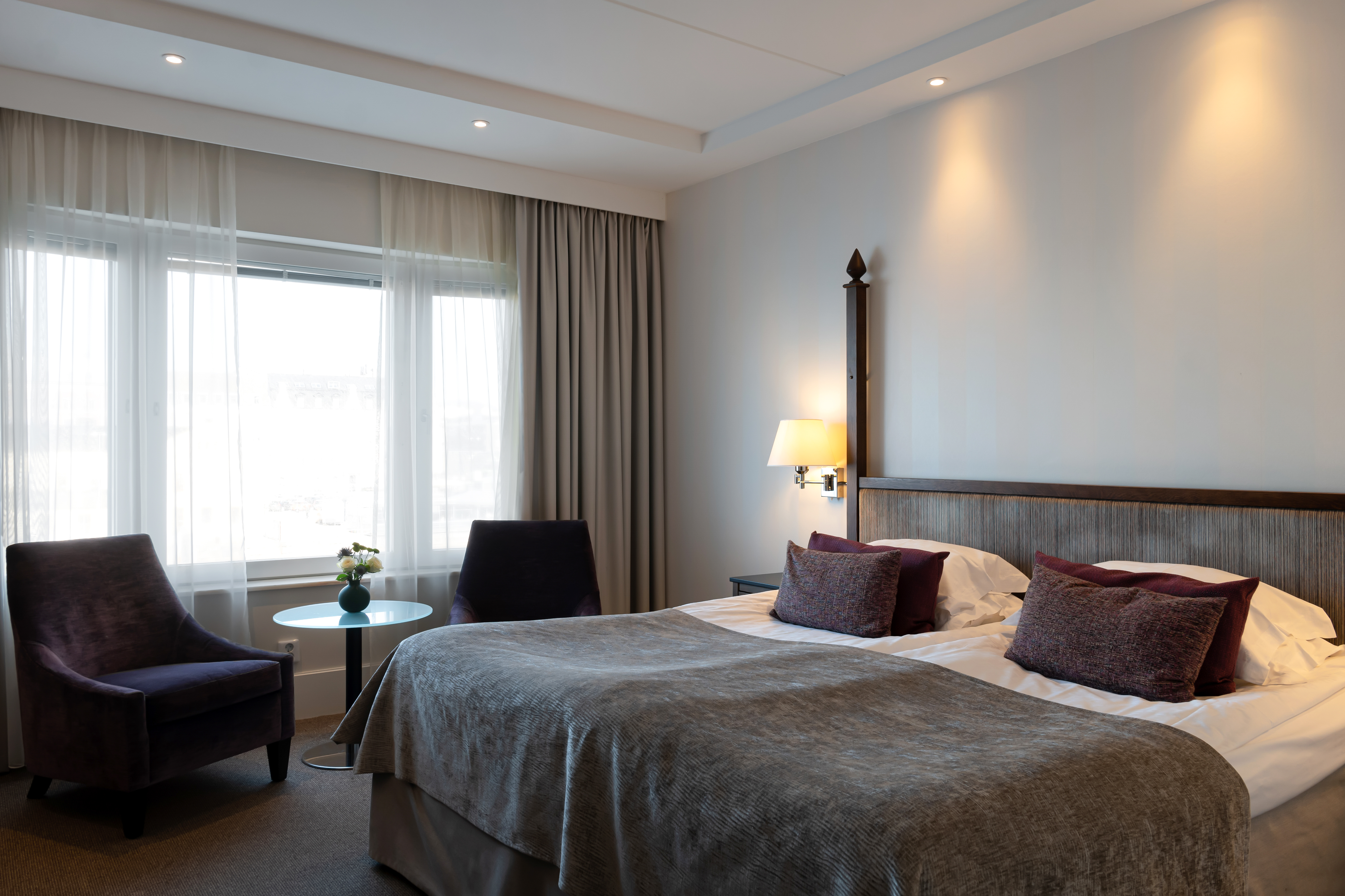 Hotel bed with silver bedspread and purple pillows