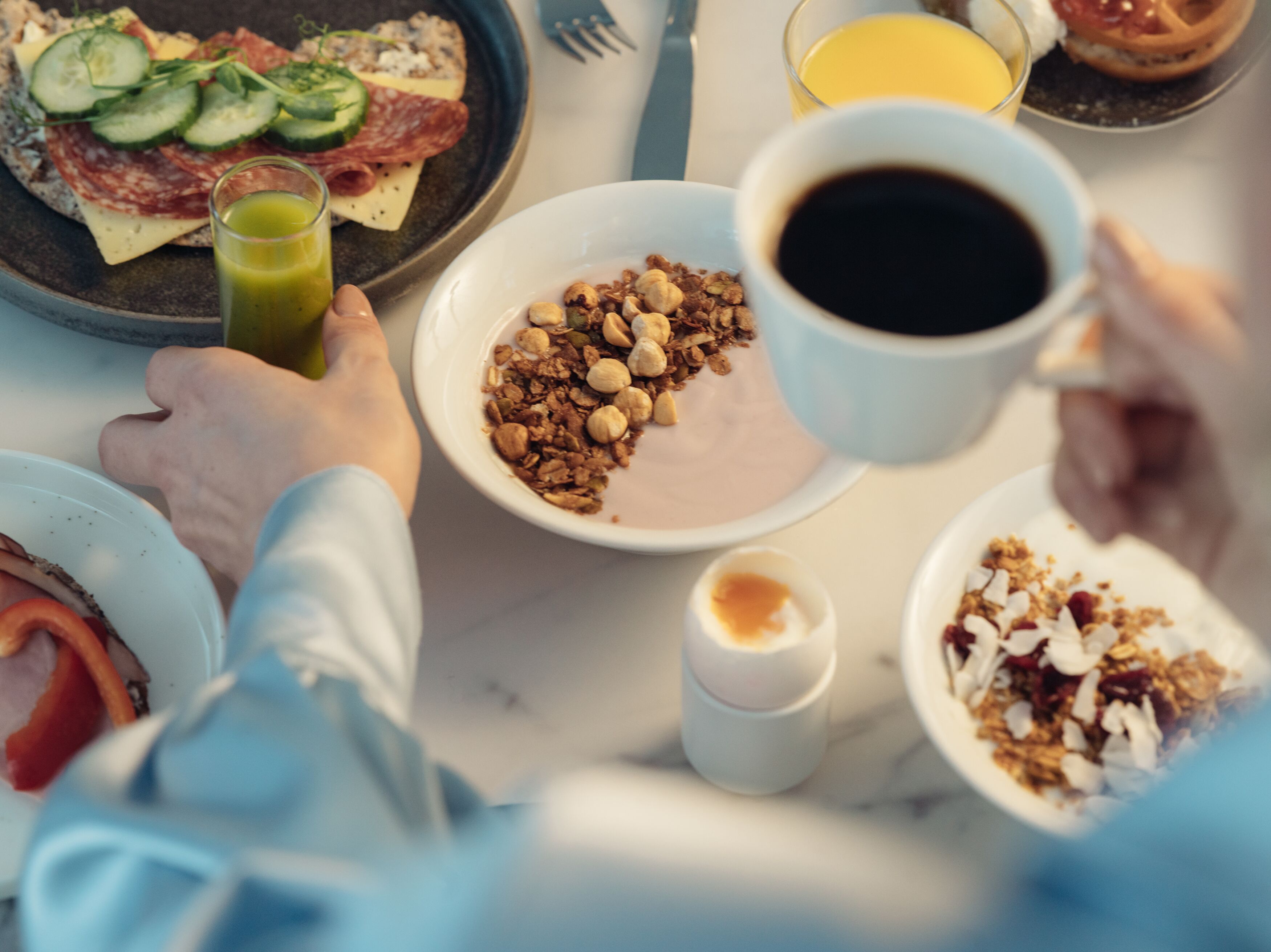 Frukostbord med kaffe, yoghurt med nötter, smörgås med kött och ost, färskpressad juice och kokt ägg.